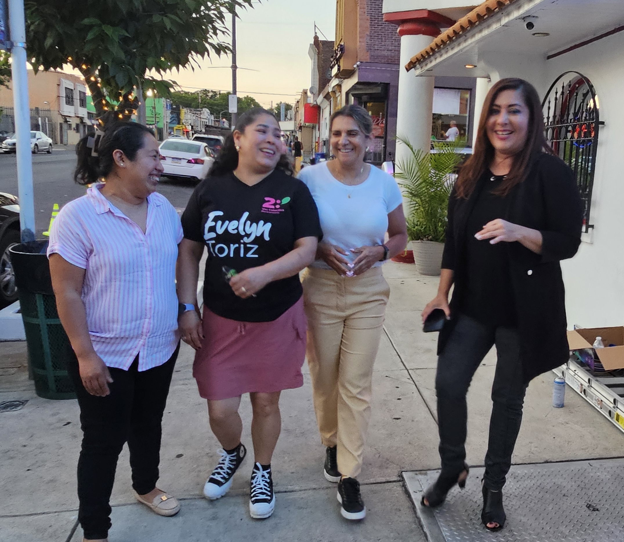 four women stand on a sidewalk and are laughing