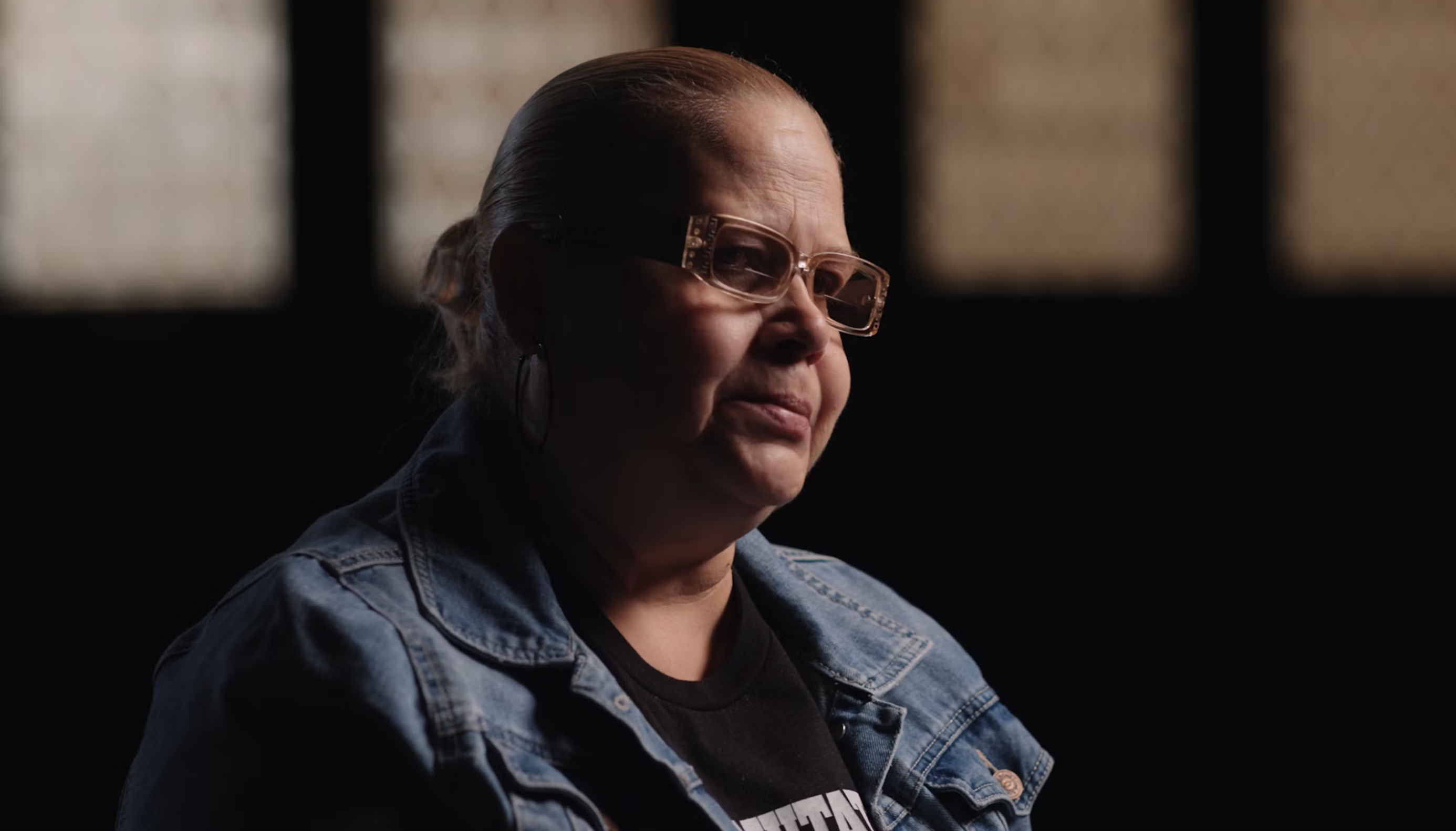 a woman wearing glasses and a blue jean jacket looks into the distance