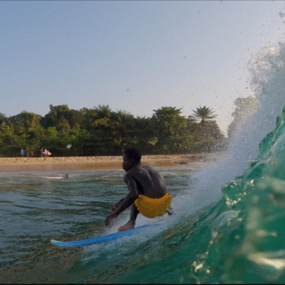 A person in yellow trunks surfing on a blue board with an island in the background