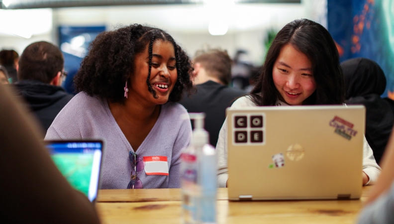 Two people seated at a table smiling at a laptop