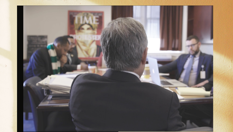 back shot of a man seated at a table having a meeting with 3 other people