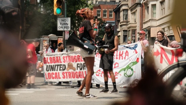 a woman holds a megaphone at a pro-Palestine rally while a man films her 
