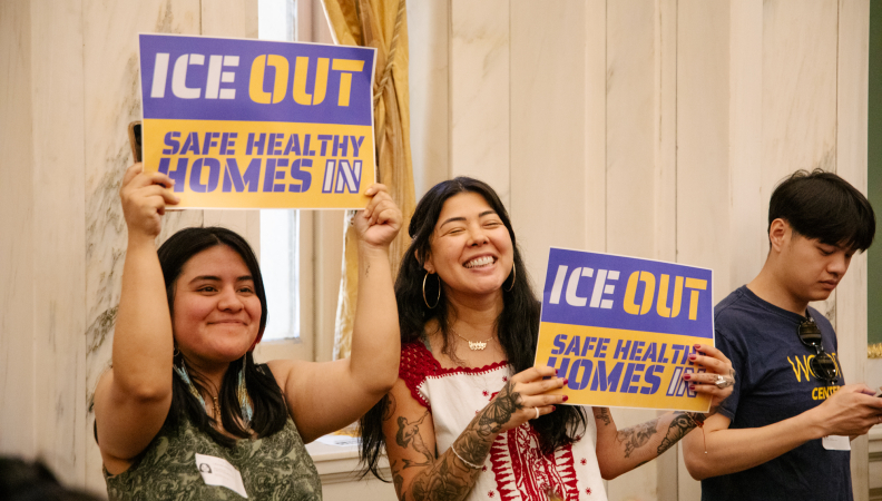 two people holding up signs that read "ICE out, safe healthy homes in."