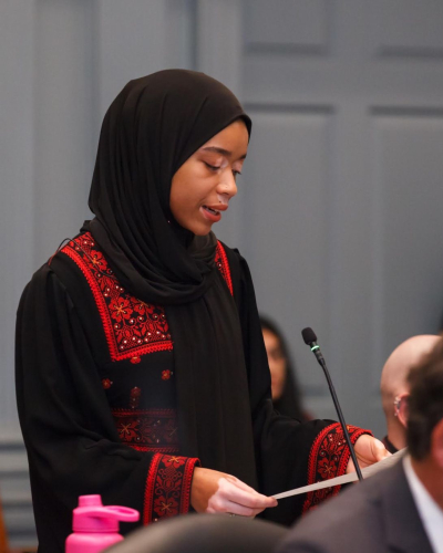 a woman wearing a hijab speaks in a congress of local Delaware politicians