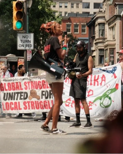 a woman holds a megaphone at a pro-Palestine rally while a man films her 