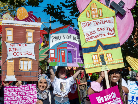 a group of protesters holding artfully made signs about the need for rent control in Philly