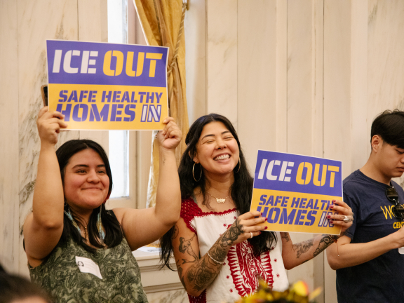 two people holding up signs that read "ICE out, safe healthy homes in."
